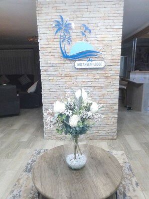 A reception area with a stone wall, a sign reading 'NOLANGENI LODGE,' and a table with a vase of flowers.