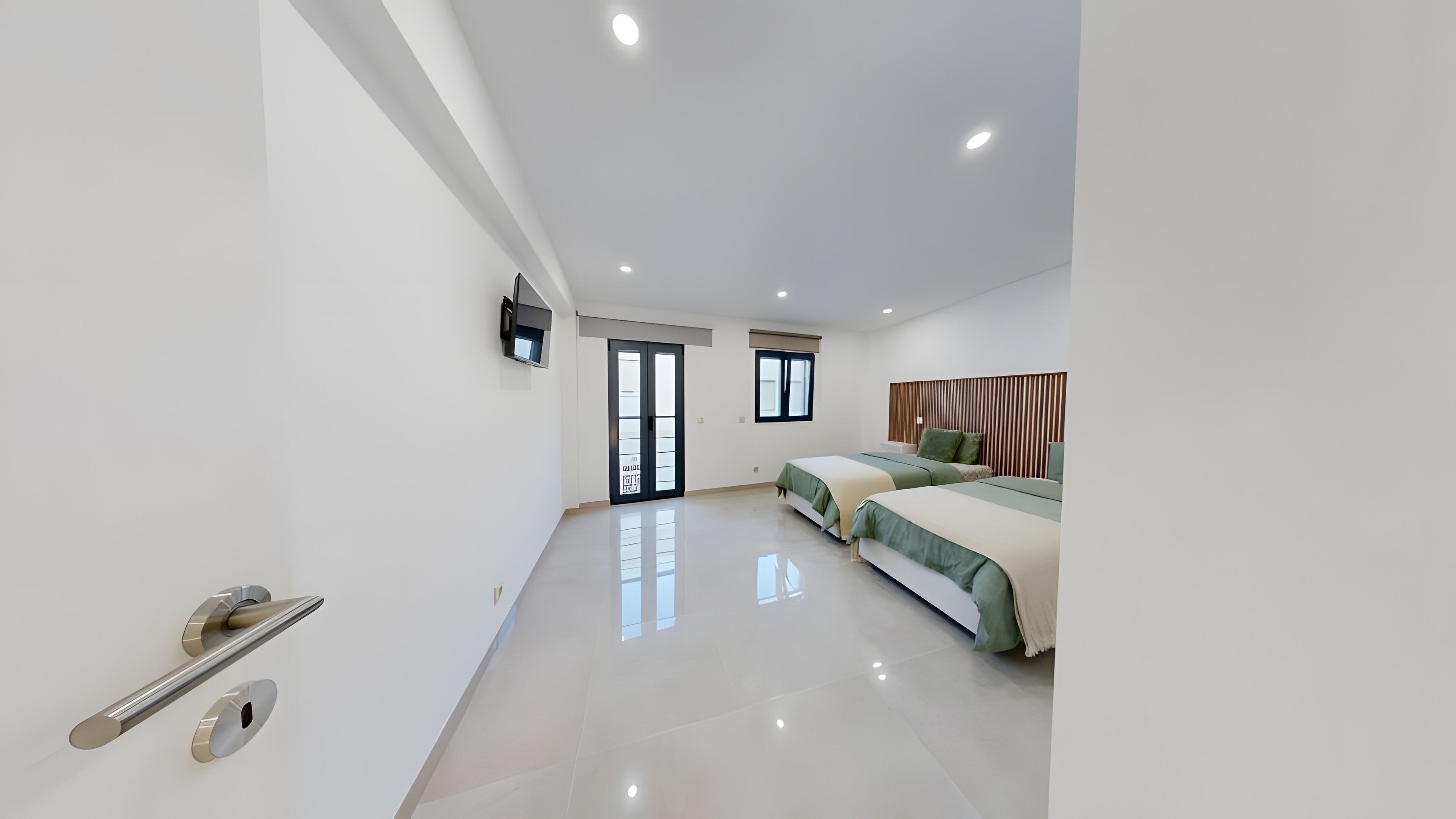 Un dormitorio moderno con una cama grande, un televisor montado en la pared y un divisor corredizo que da a otra habitación.