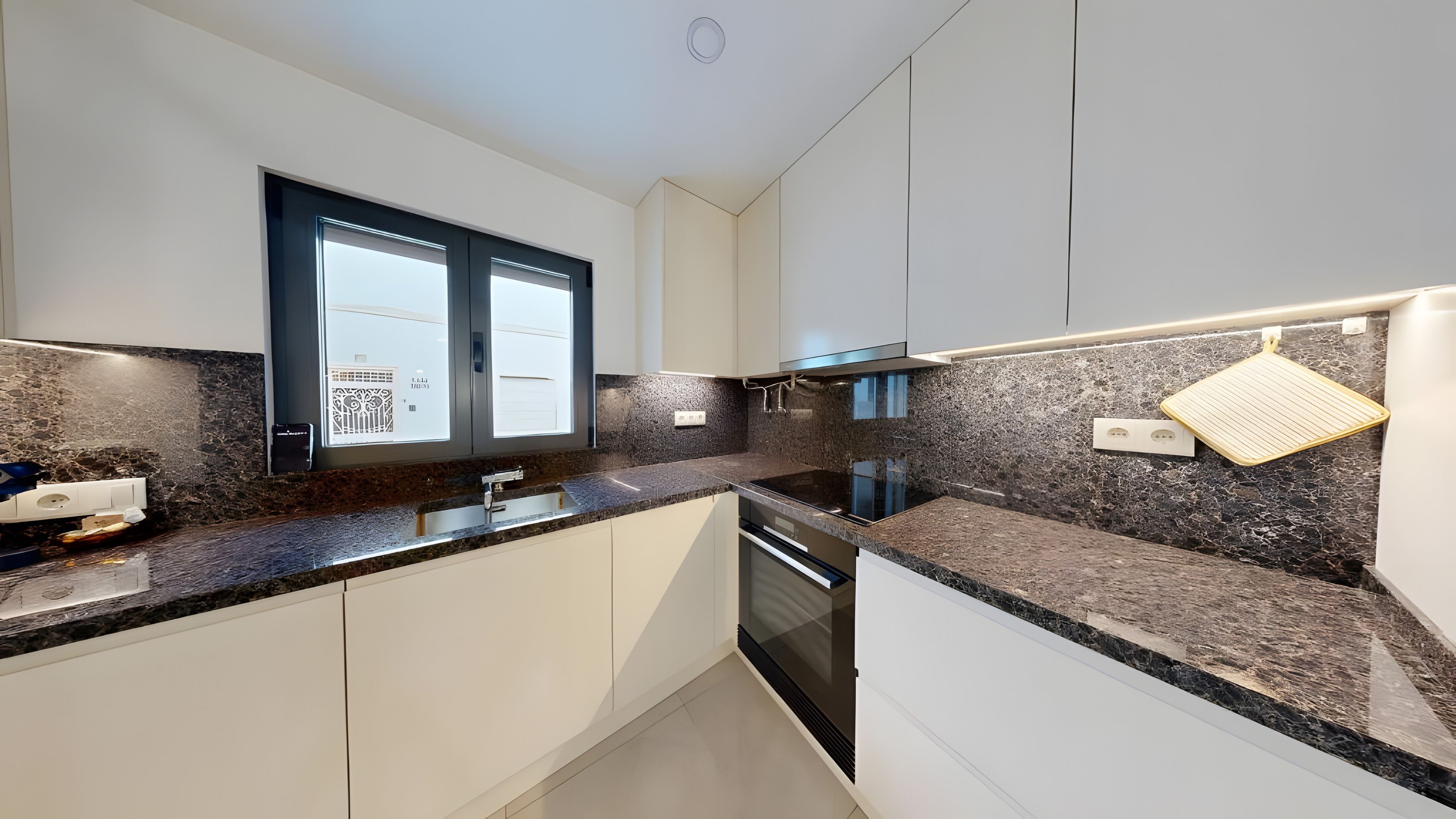 Een moderne keuken met granieten werkbladen, roestvrijstalen apparatuur en witte kastjes.