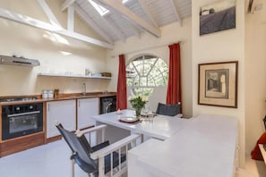 Eine kompakte Küche mit Essecke, einem Fenster mit roten Vorhängen und einem gerahmten Bild an der Wand.