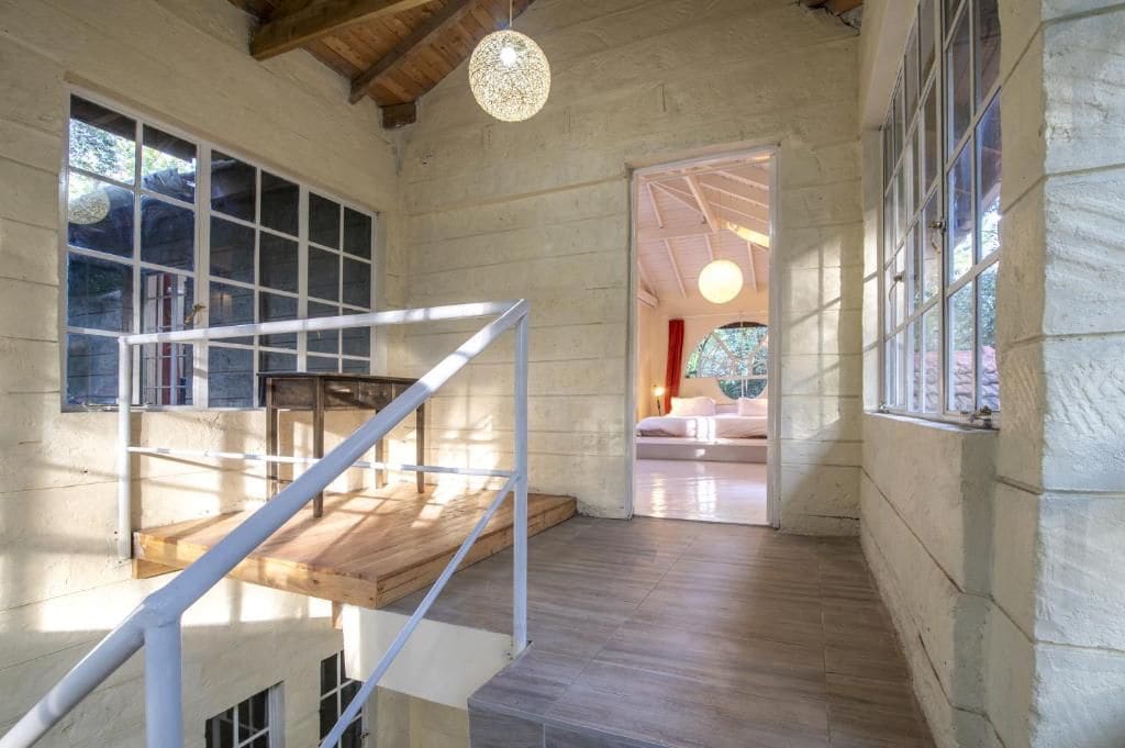 Una escalera de madera que conduce a un balcón con vista a una habitación con una cama y una lámpara colgante.