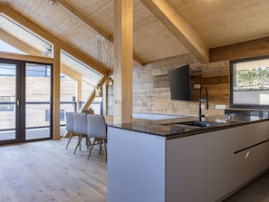 Eine moderne Küche mit einer großen Kochinsel, Holzbalken und einem an der Wand befestigten Flachbildfernseher.