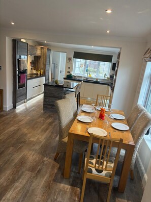 A dining area with a wooden table set for four, a kitchen in the background, and a view of the outdoors through a window. - Close to marinas and town.  Large downstairs areas & 3 bedrooms and 3 bathrooms. (Cowes)