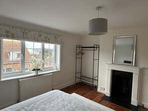 A bedroom with a bed, a radiator, a window with a view of buildings, a hanging light fixture, a metal rack, and a fireplace. - Close to marinas and town.  Large downstairs areas & 3 bedrooms and 3 bathrooms. (Cowes)