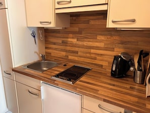 Eine kleine Küche mit einer Holz Arbeitsplatte, einem eingebauten Herd, einer Spüle und weißen Schränken.