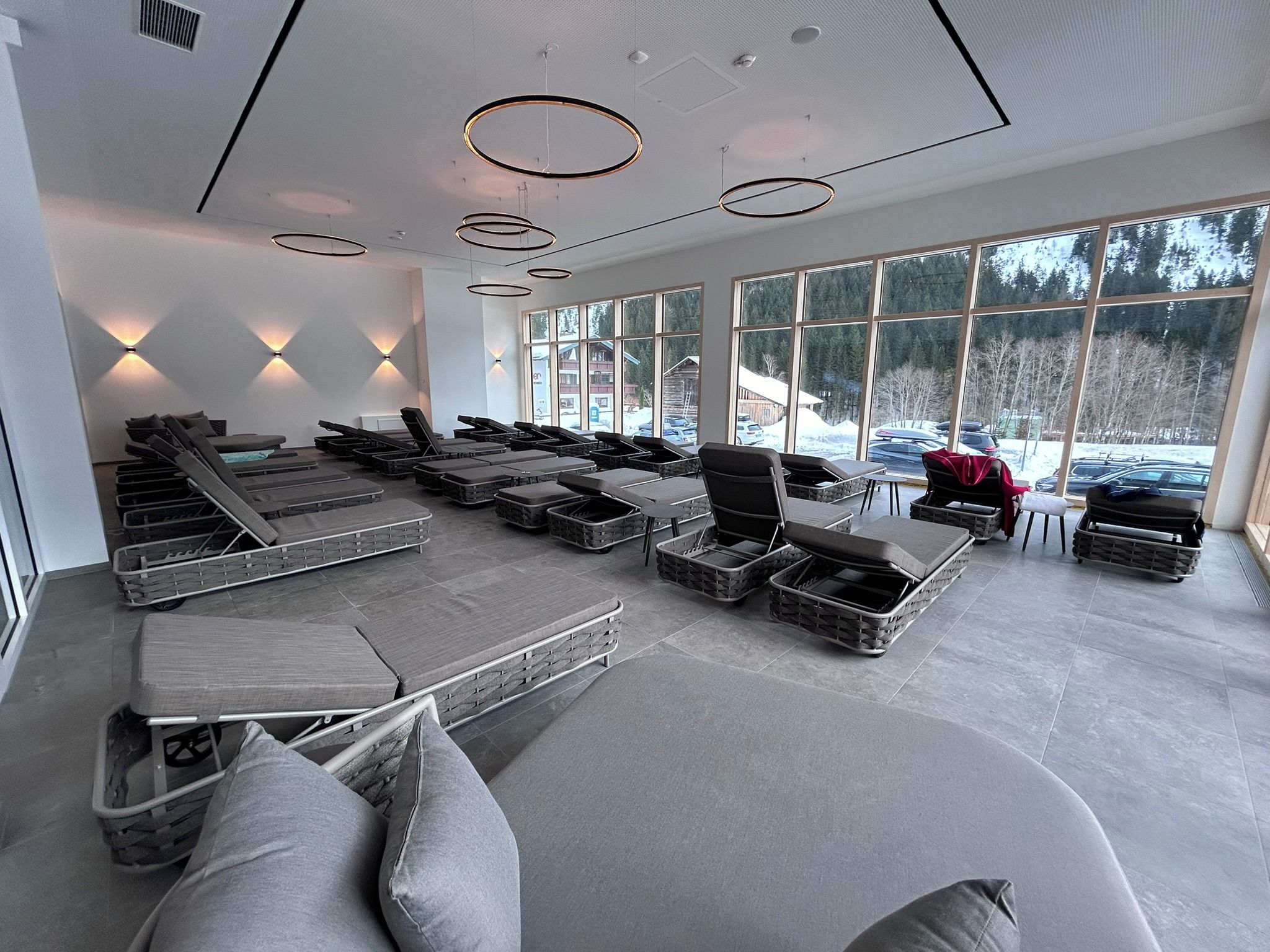 A modern spa room with multiple massage tables, a large window with a view of the outside, and a ceiling with circular light fixtures.