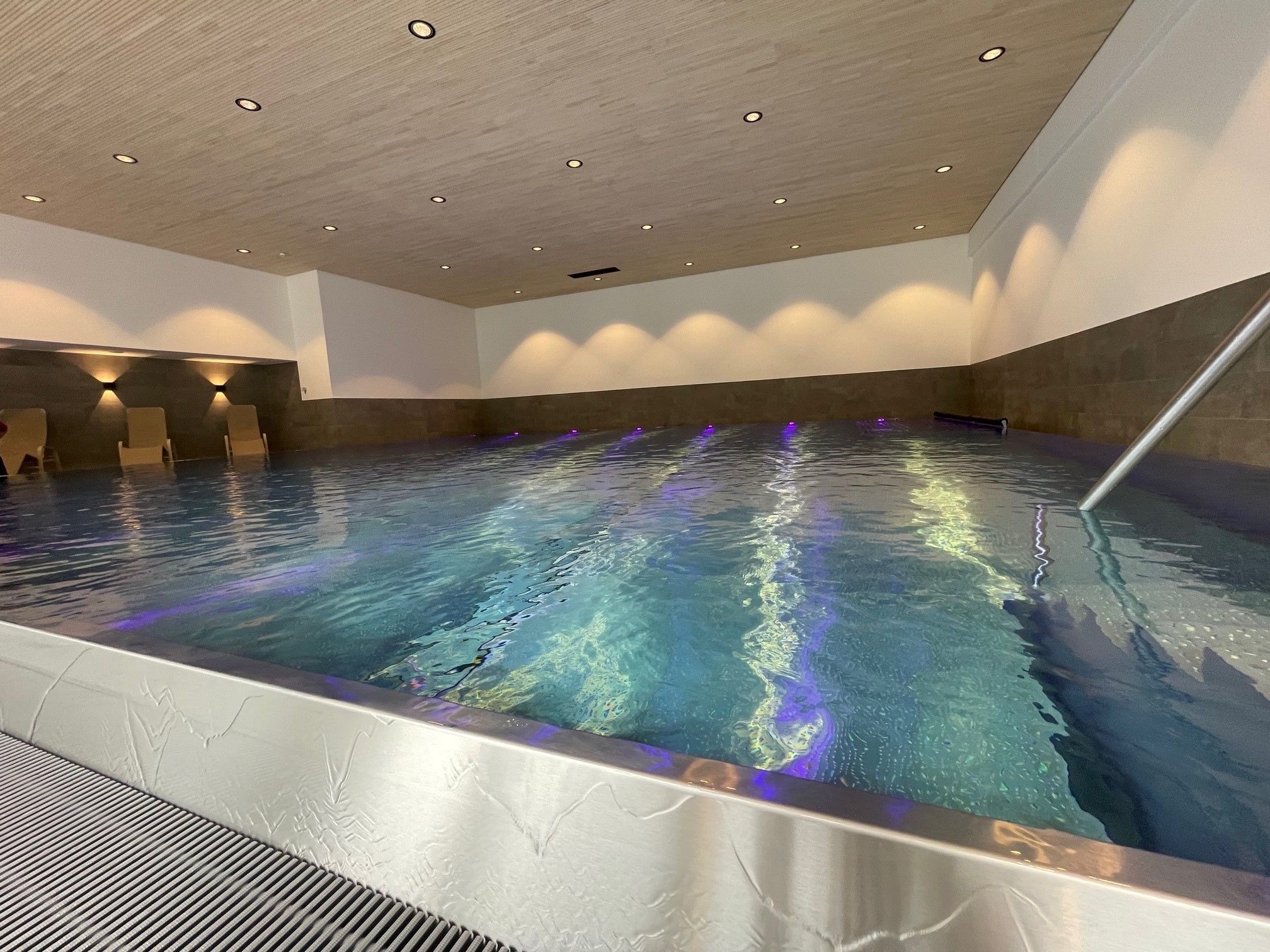 Ein heller, überdachter Pool mit klarem Wasser, Holzbalkendecke und modernem Design.
