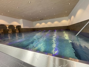 An indoor swimming pool with a wooden ceiling and wall, and a metal pool edge. - Vrbo Property (Mittelberg)