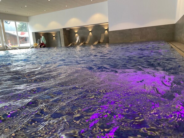 Ein großes Hallenbecken mit spiegelnder Oberfläche und violetter Beleuchtung.