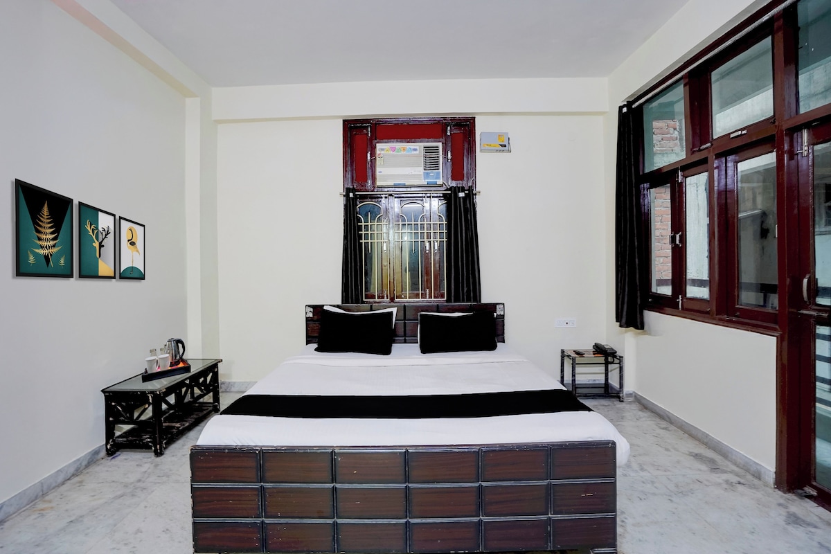 Una camera da letto con un letto, un tavolino con bollitore, una finestra con tende e opere d'arte appese al muro.