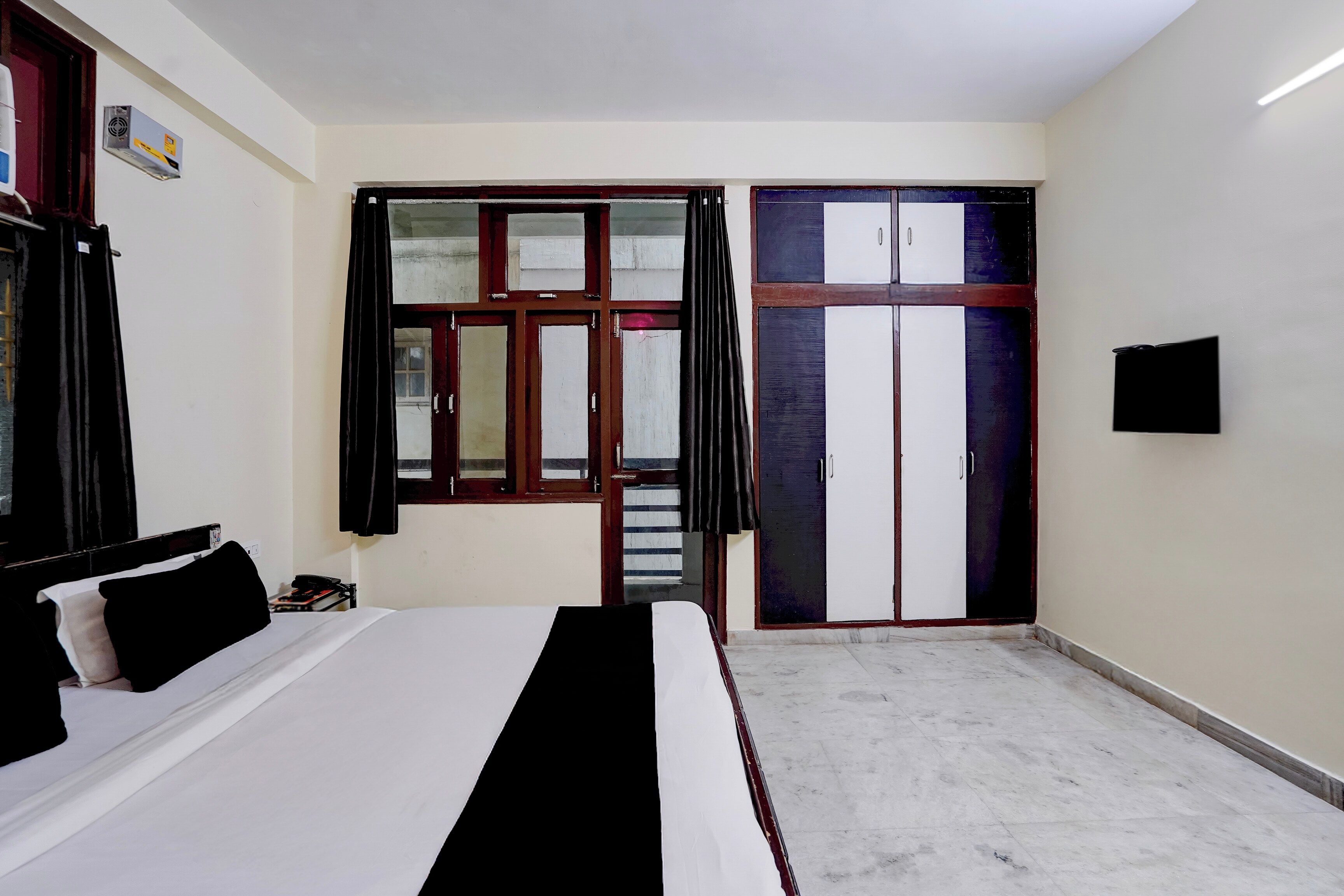 A bedroom with a bed, a wardrobe, a television, and a window with curtains.