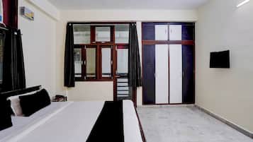 A bedroom with a bed, a wardrobe, a television, and a window with curtains.