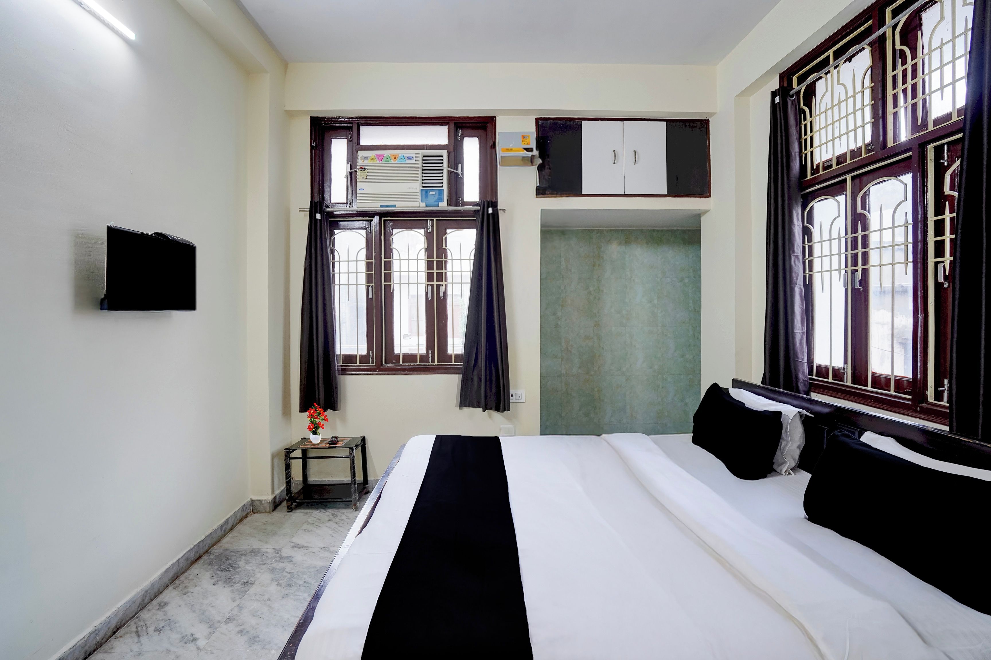 Un dormitorio con una cama, un armario, una mesita con flores y un televisor en la pared.