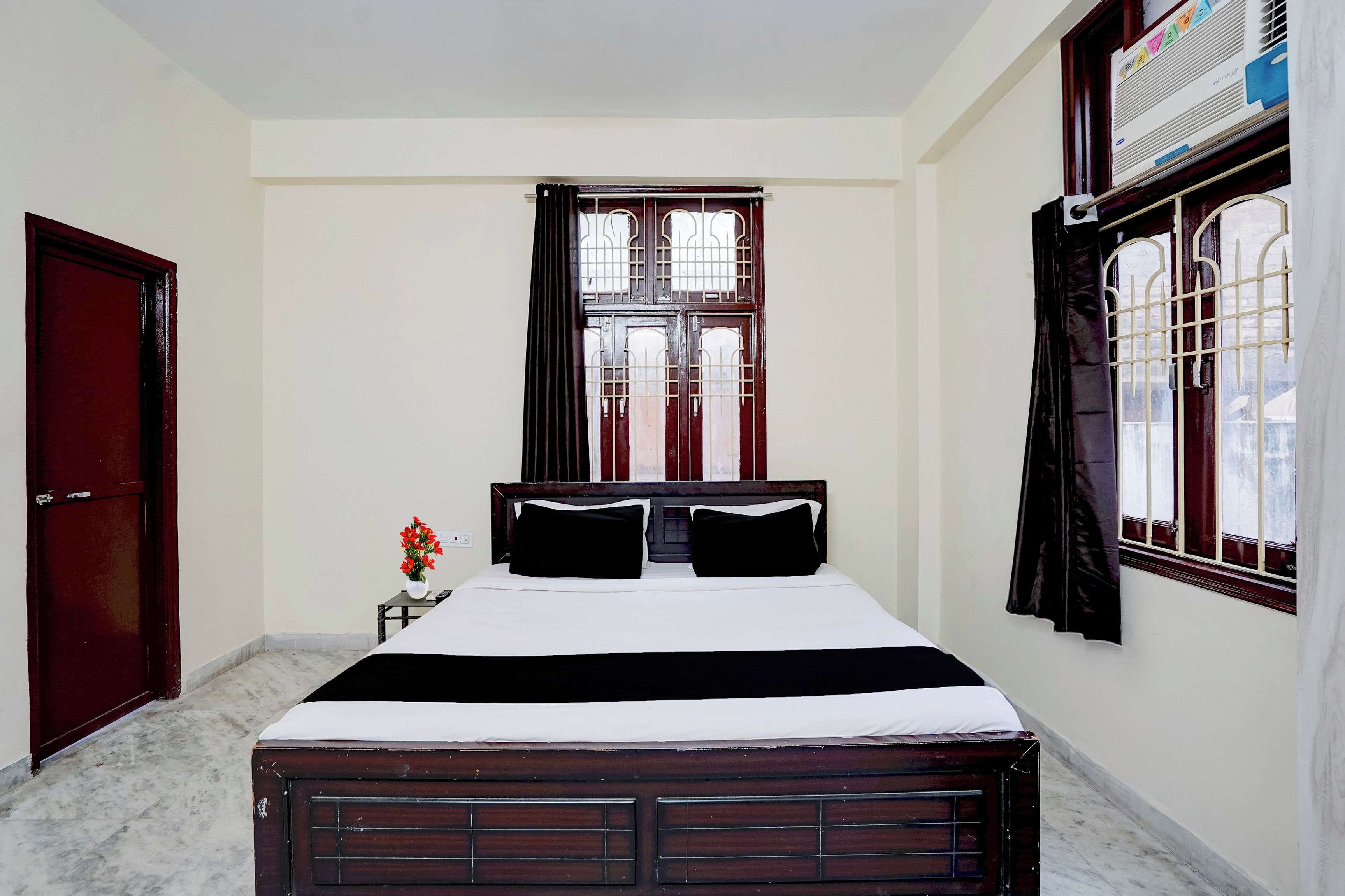 Un dormitorio con cama, ventana con cortinas, radiador y puerta.