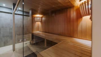 A sauna with wooden walls and a glass door, a bench, and a wall-mounted light fixture.