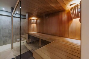 Un sauna avec des murs en bois, une porte en verre, un banc et un luminaire fixé au mur.