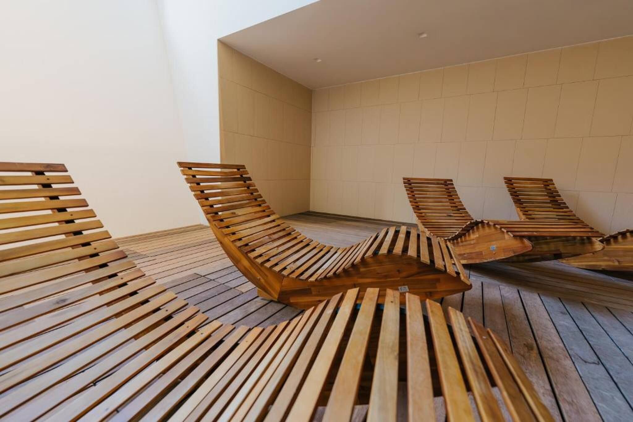 Una habitación con sillones reclinables de listones de madera dispuestos sobre un piso de madera, frente a una pared lisa.
