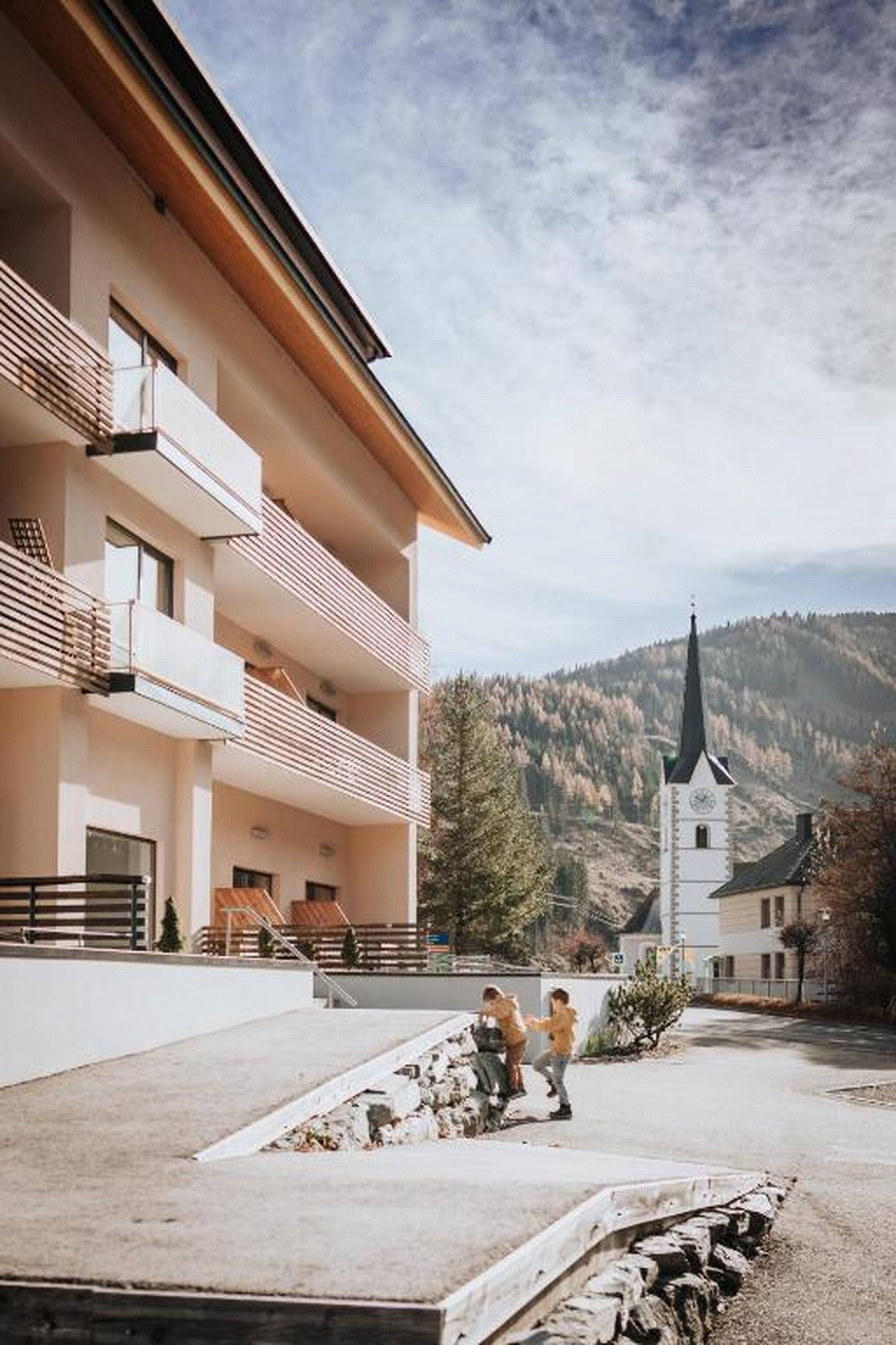 Ein mehrstöckiges Gebäude mit Balkonen, einem gepflasterten Innenhof und einer Kirche im Hintergrund.