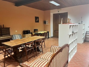 A dining area with a wooden table and chairs, a sofa, a white shelving unit, and a kitchen area with cabinets and a stove. - Casa Stabbi with Mountain View, Private Garden, and Air Conditioning (Chitignano)