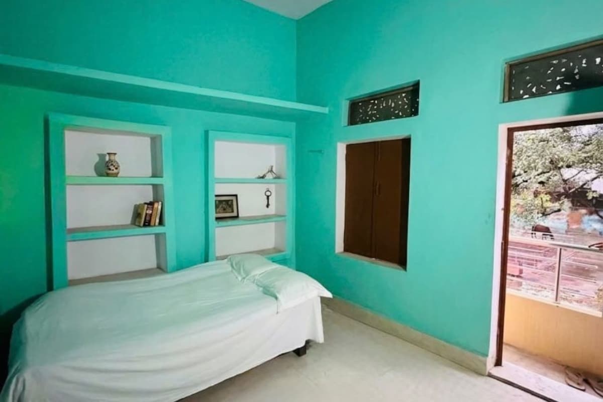 Una habitación con paredes verde azulado, una cama, un armario y una ventana con vista al exterior.