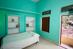 Una habitación con paredes verde azulado, una cama, un armario y una ventana con vista al exterior.
