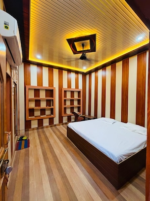 Una habitación con cama, estantes empotrados, ventilador de techo y piso de madera.