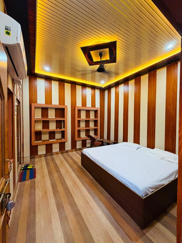 A room with a bed, built-in shelves, a ceiling fan, and a wooden floor. - Malti Homestay (Varanasi)