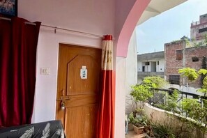 A room with a wooden door, red curtains, and a balcony with potted plants. - Malti Homestay (Varanasi)