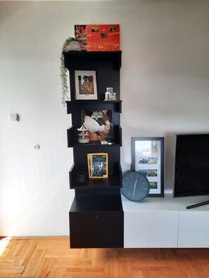 A black shelving unit with various items including a framed picture, a clock, and a book. - Cozy 1-bedroom apartment in tranquil Skopje with AC and free parking (Skopje)