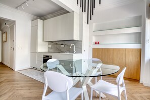 A modern kitchen with white cabinets, a glass dining table, and white chairs. - Whitewood Residence (Athina)