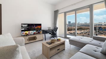 Un salon moderne avec un grand téléviseur, un ordinateur portable posé sur un bureau et une vue sur le paysage urbain, visible à travers de grandes fenêtres.
