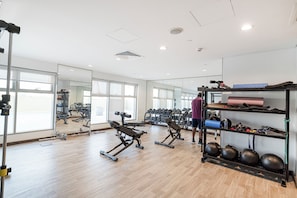 A gym with exercise equipment, a mirror, and a shelf with bags and water bottles. - Cozy 1BHK in Rabdan Motor City Dubai (Dubai)