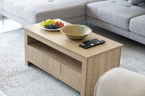 A wooden coffee table with a bowl and a remote control on top, a grey sofa in the background, and a patterned rug on the floor. - Cozy 1BHK in Rabdan Motor City Dubai (Dubai)