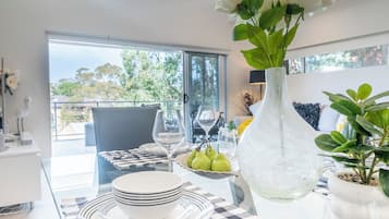 Un coin repas avec une table dressée pour deux personnes, un vase rempli de fleurs et une vue sur l’extérieur.