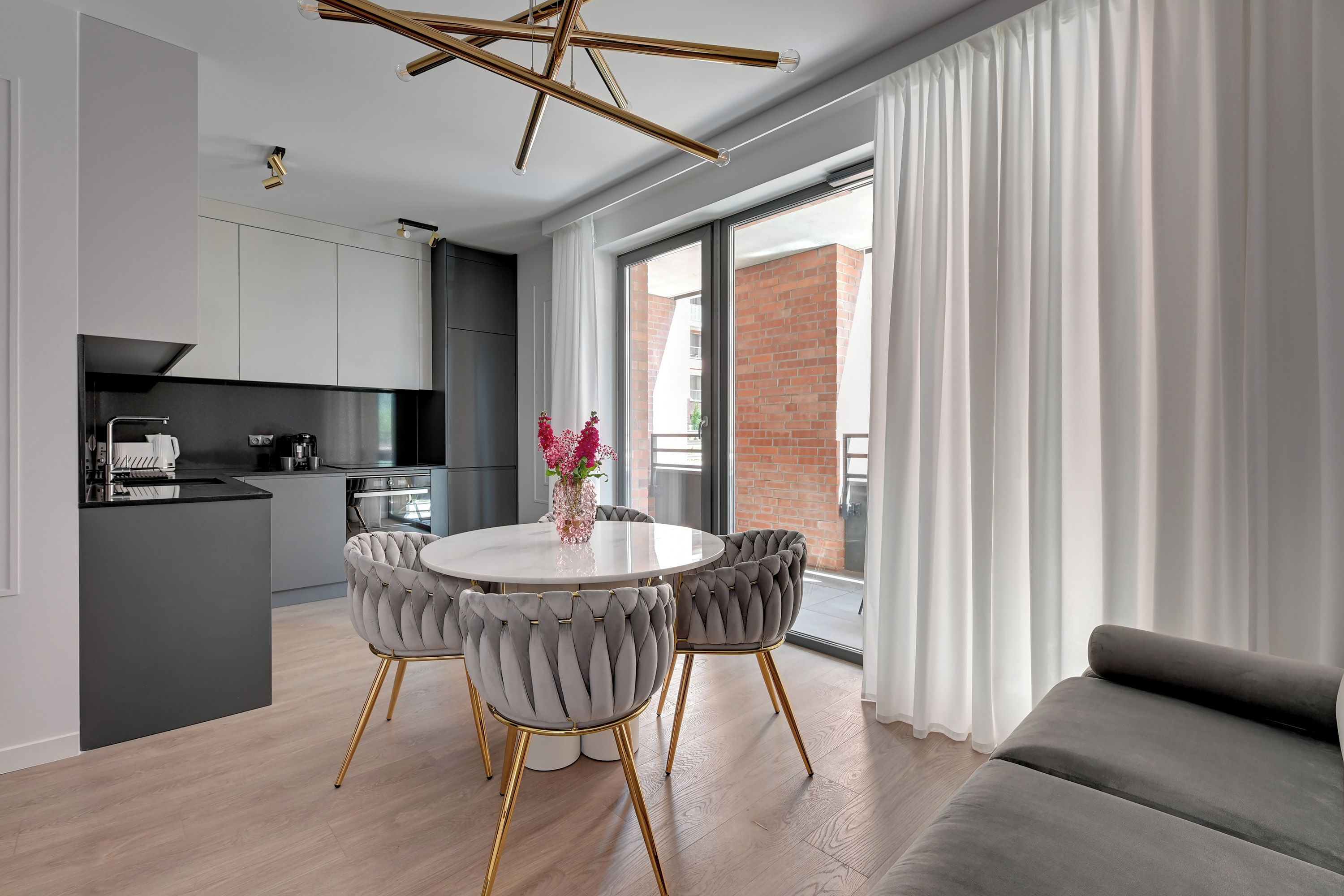 A modern kitchen with a dining area, featuring a round table with chairs and a vase of flowers.
