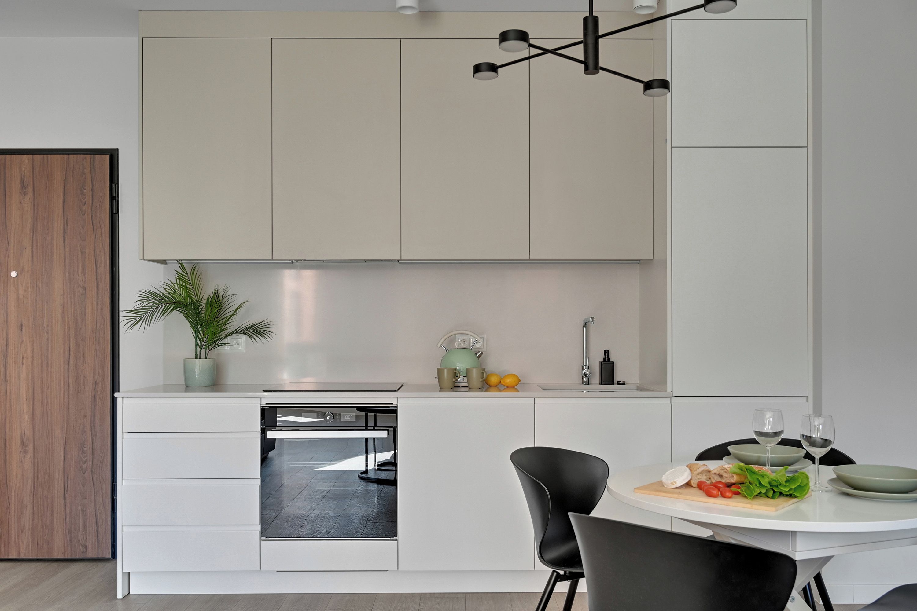 A modern kitchen with white cabinetry, a built-in dishwasher, a dining table with chairs, and a pendant light fixture.