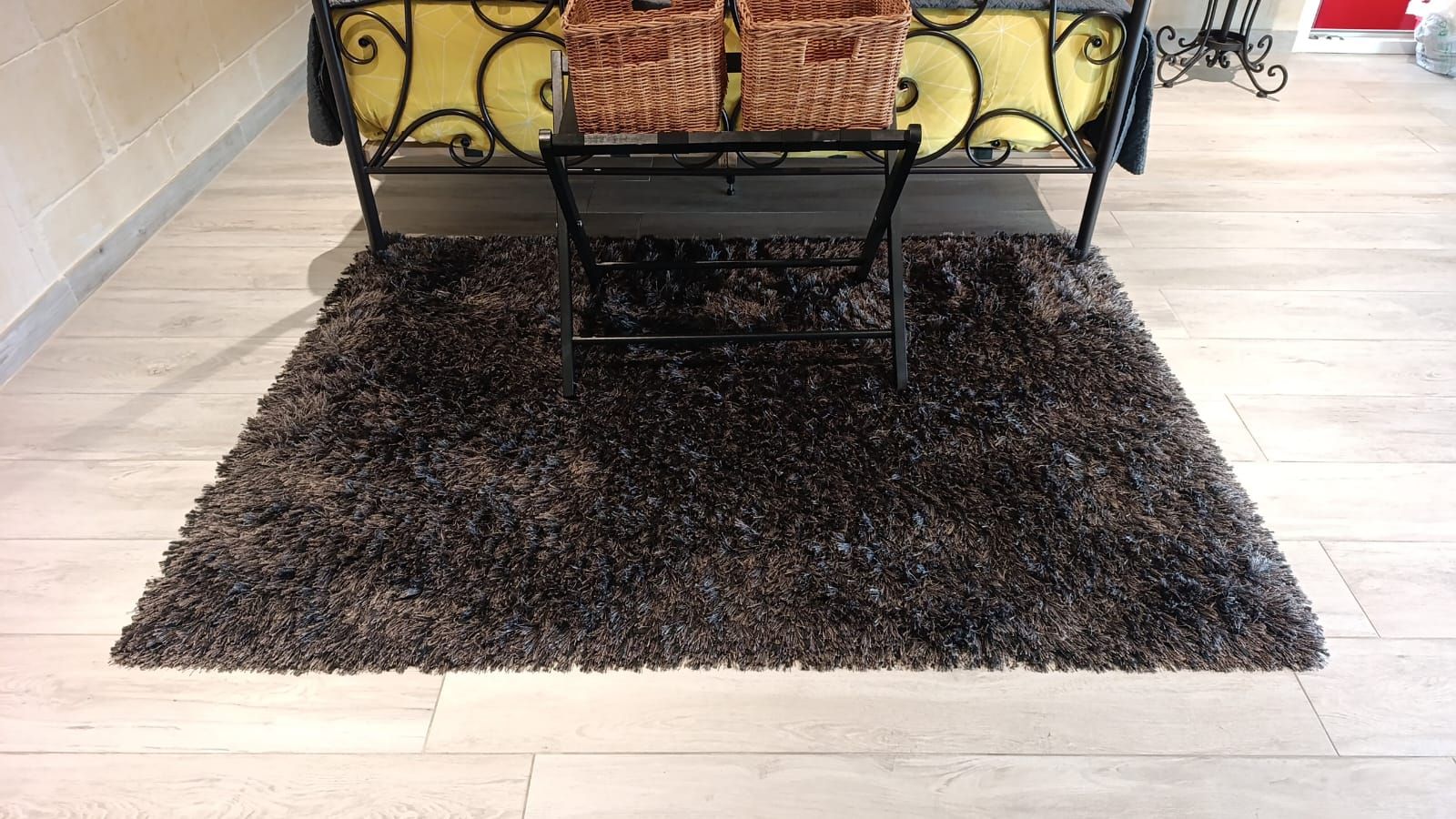 Ein Zimmer mit einem Bett, einem dunklen Teppich mit Struktur und einem hellen Holzboden.