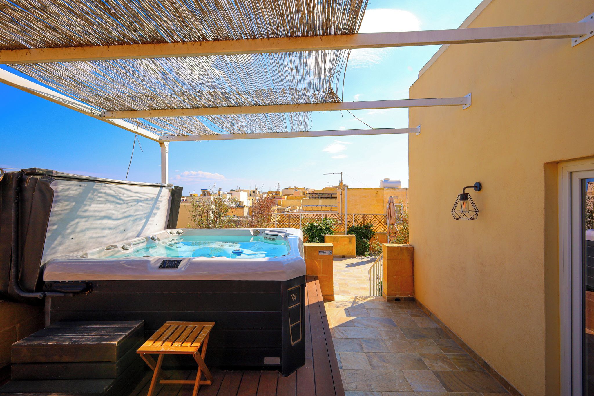 A hot tub with a wooden bench, a pergola overhead, and a view of the cityscape.