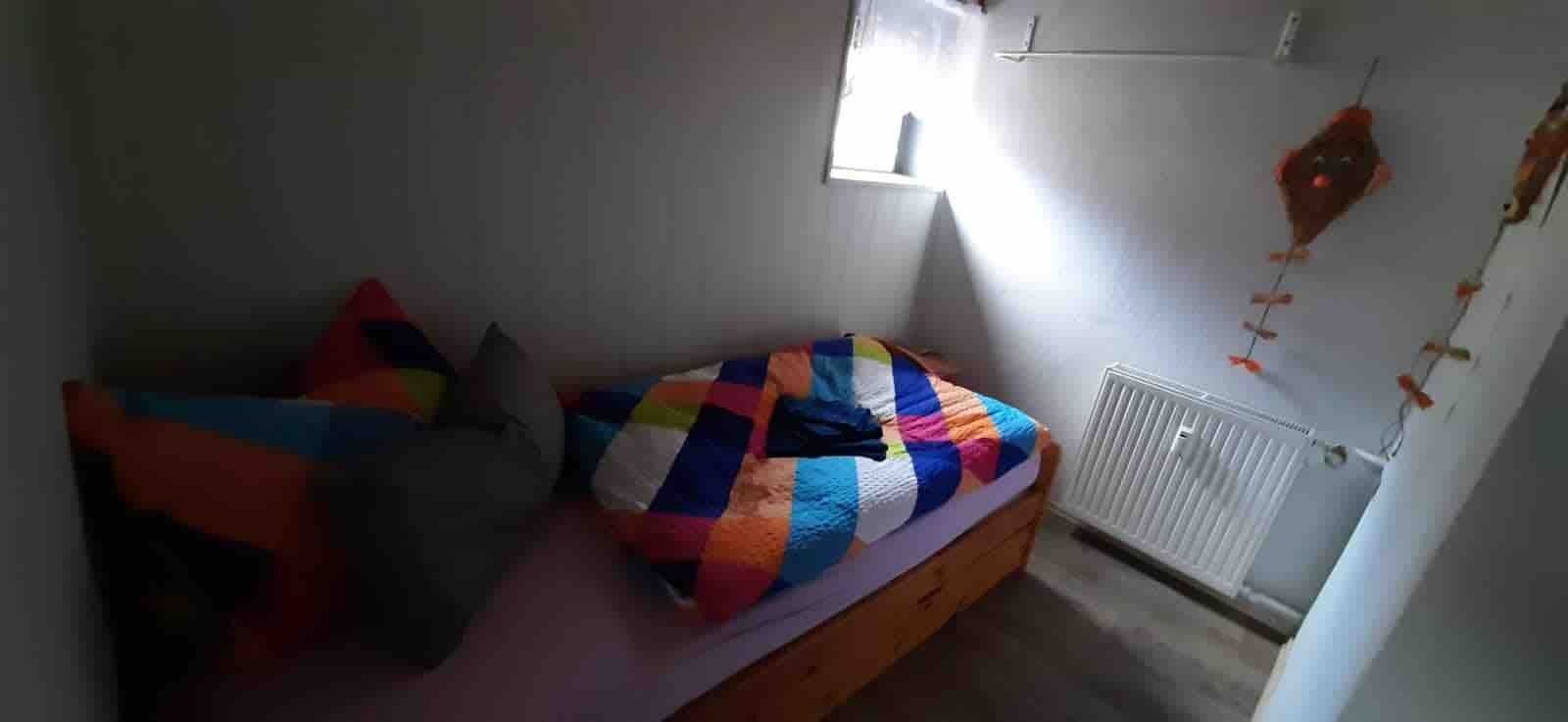 Une chambre à coucher avec un lit, des oreillers, un radiateur et une fenêtre.