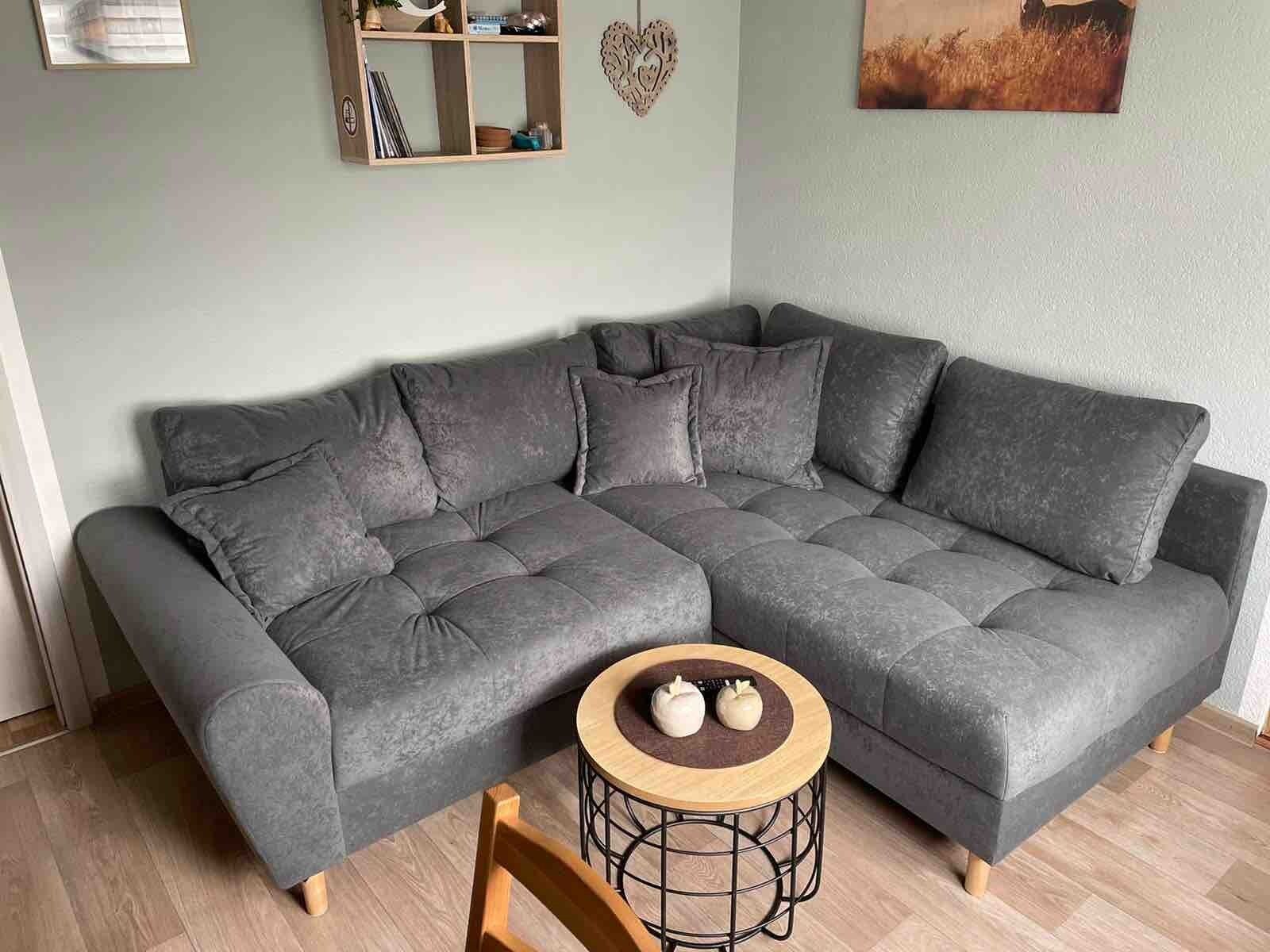 A sectional sofa with a round wooden side table in a room with light-colored walls and wooden flooring.