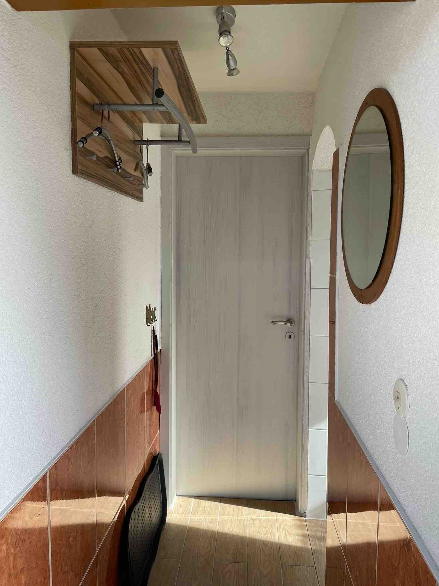 Una habitación con puerta blanca, techo de madera, espejo y suelo de baldosas.