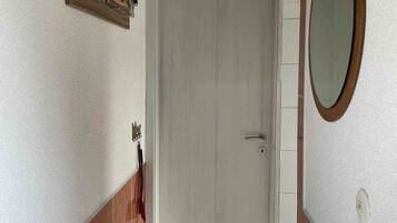 Una habitación con puerta blanca, techo de madera, espejo y suelo de baldosas.