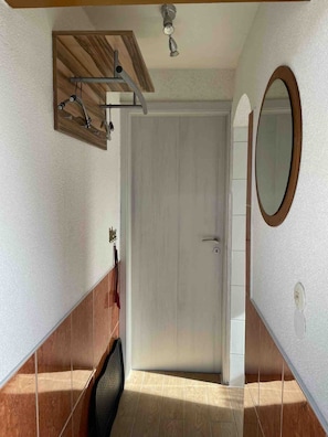 Una habitación con puerta blanca, techo de madera, espejo y suelo de baldosas.