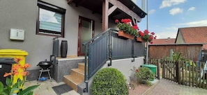 Un edificio residencial con fachada gris, cerca de madera y balcón con flores rojas.