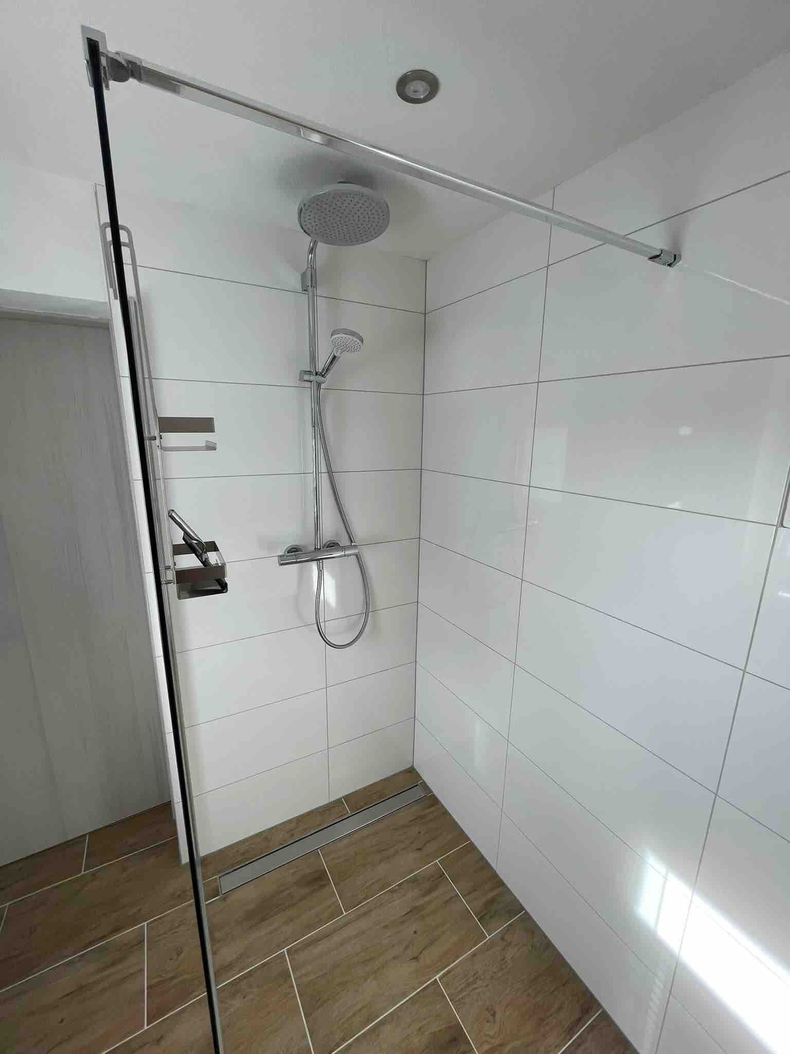 Eine Dusche mit Glastür, Duschbrause und Armatur an der Wand.