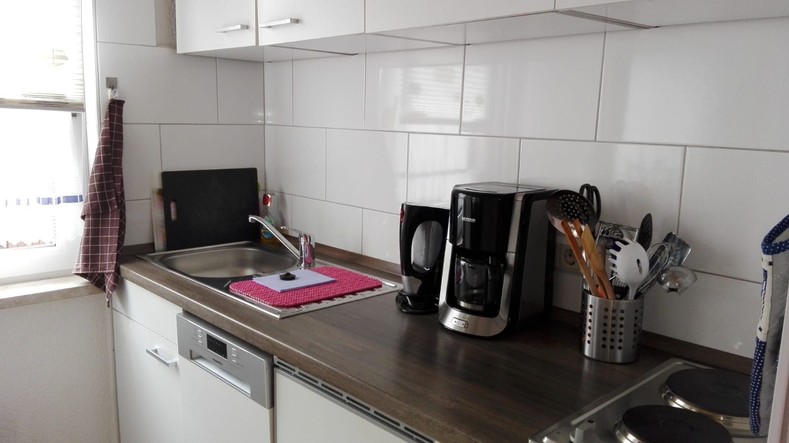 Eine moderne Küche mit einer Edelstahlspüle, einer Kaffeemaschine und einem Besteckhalter.