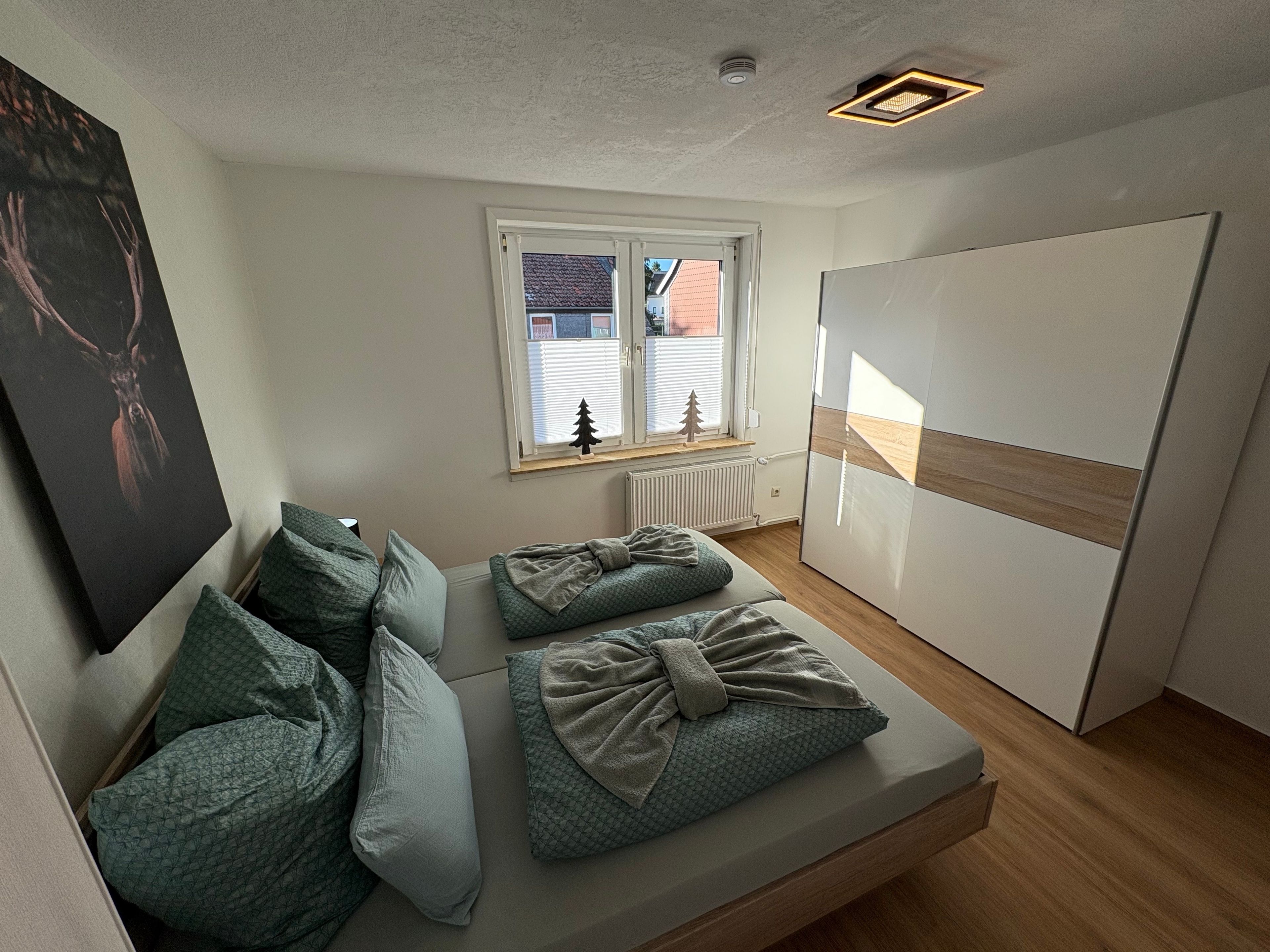 A modern bedroom with a bed, pillows, a window with blinds, a radiator, and a wardrobe.