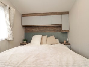 A bedroom with a bed, a wooden headboard, a nightstand, and a potted plant. - Brookwood Willerby, 36 Bay View (Filey)
