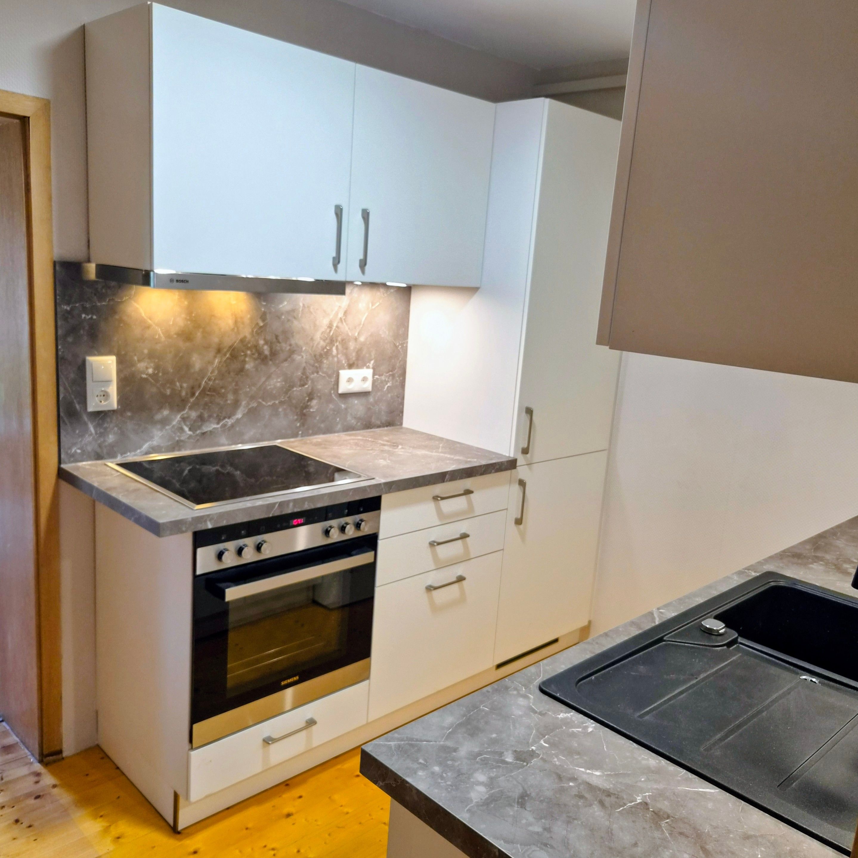 A kitchen with a built-in oven, a stovetop, and white cabinets.