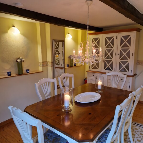 A dining room with a wooden table, white chairs, a chandelier, and a cabinet with glass doors.